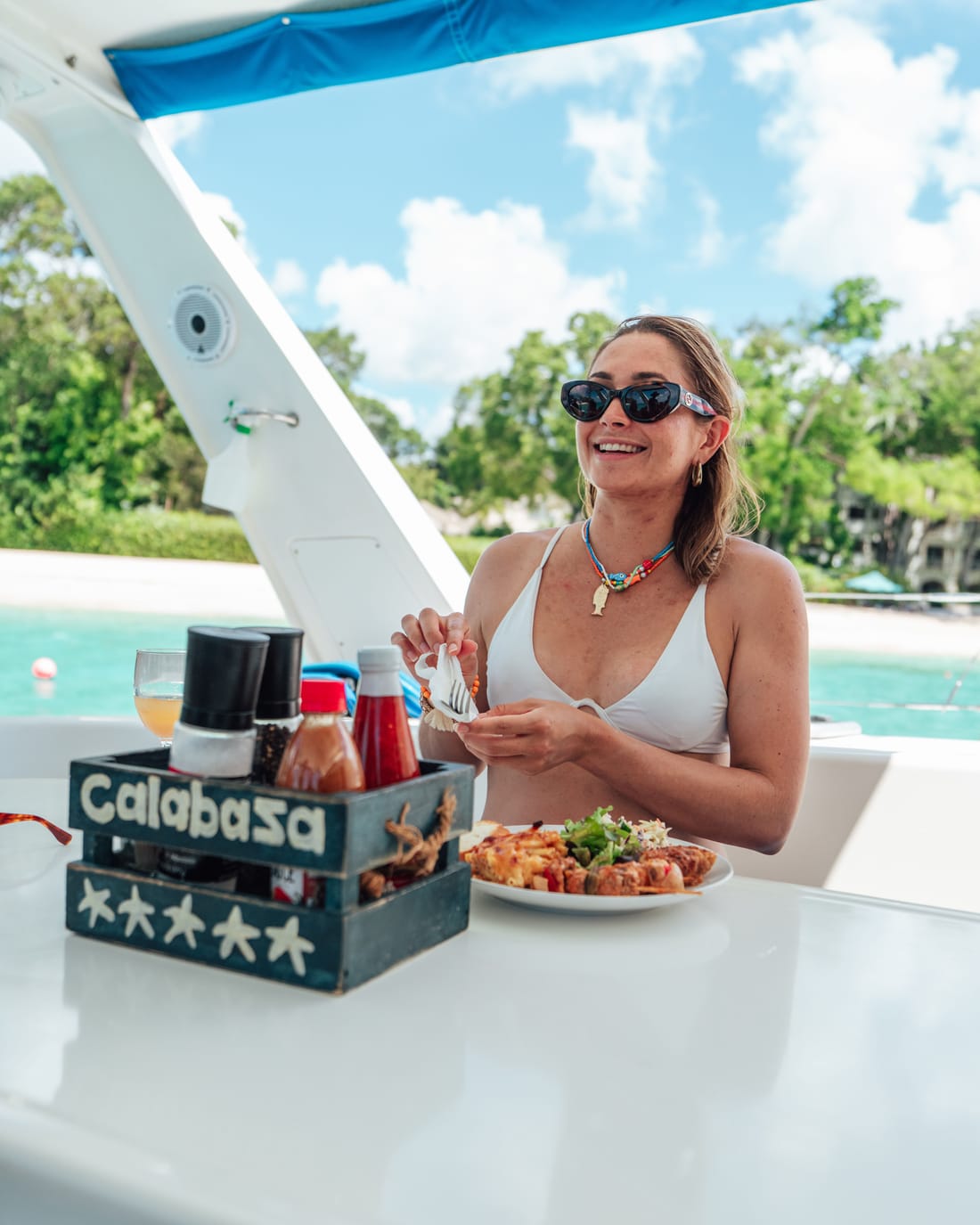 A guest smiling over a plate of lunch on deck, the Calabaza table caddy beside her