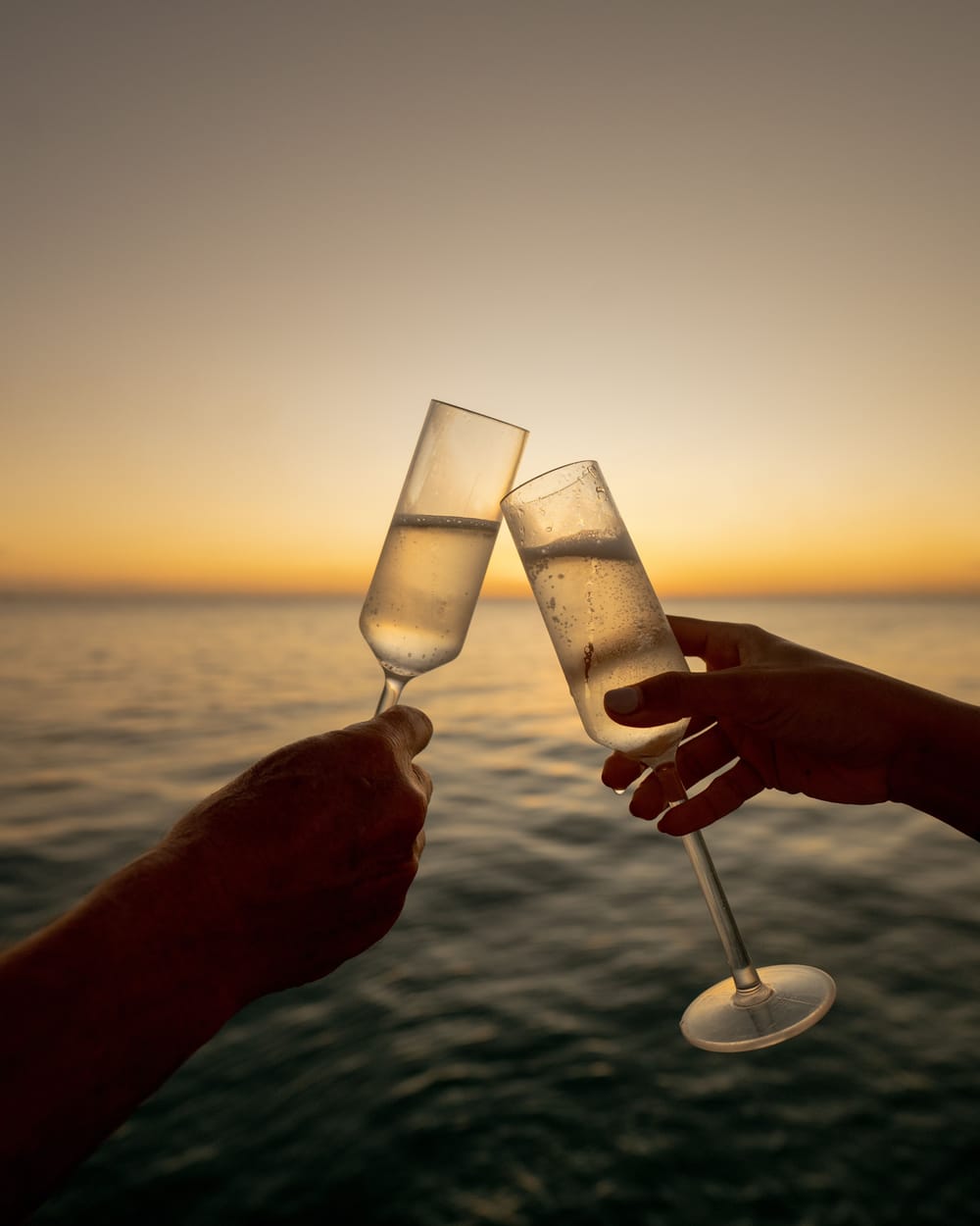 Two glasses of bubbly raised against a golden sunset over the sea