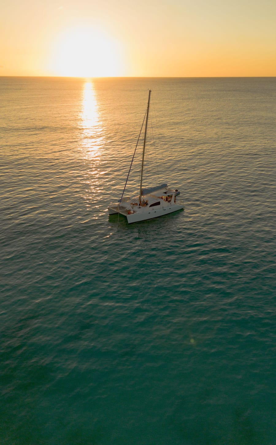 Calabaza under sail on calm water as the sun sets, seen from above