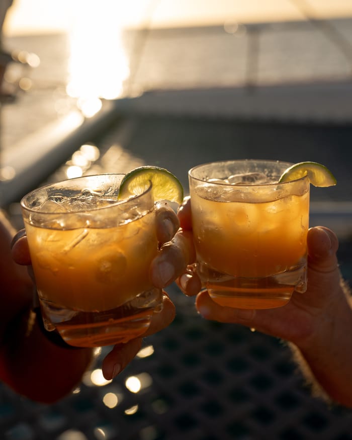 Two glasses of rum punch with lime raised together in the late sun
