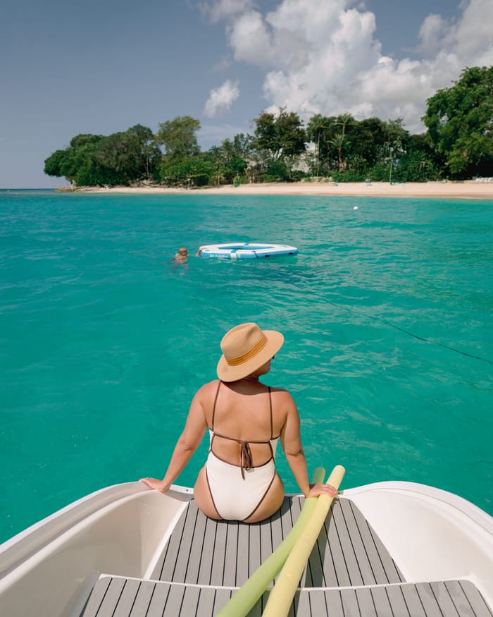 A guest in a sun hat sitting on the bow, looking toward the beach and palm trees