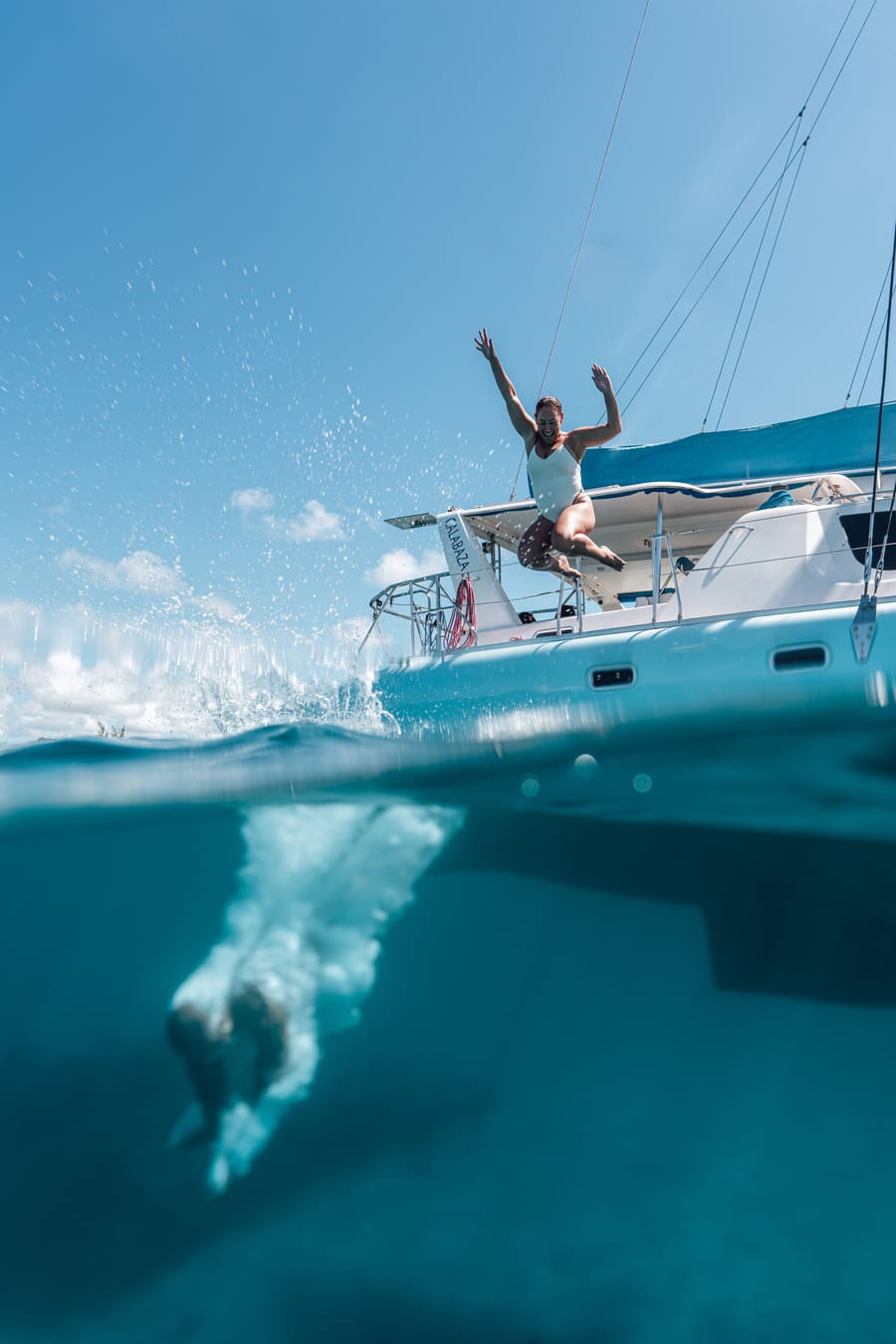 Split view at the waterline: a guest jumps from the bow and the splash continues underwater